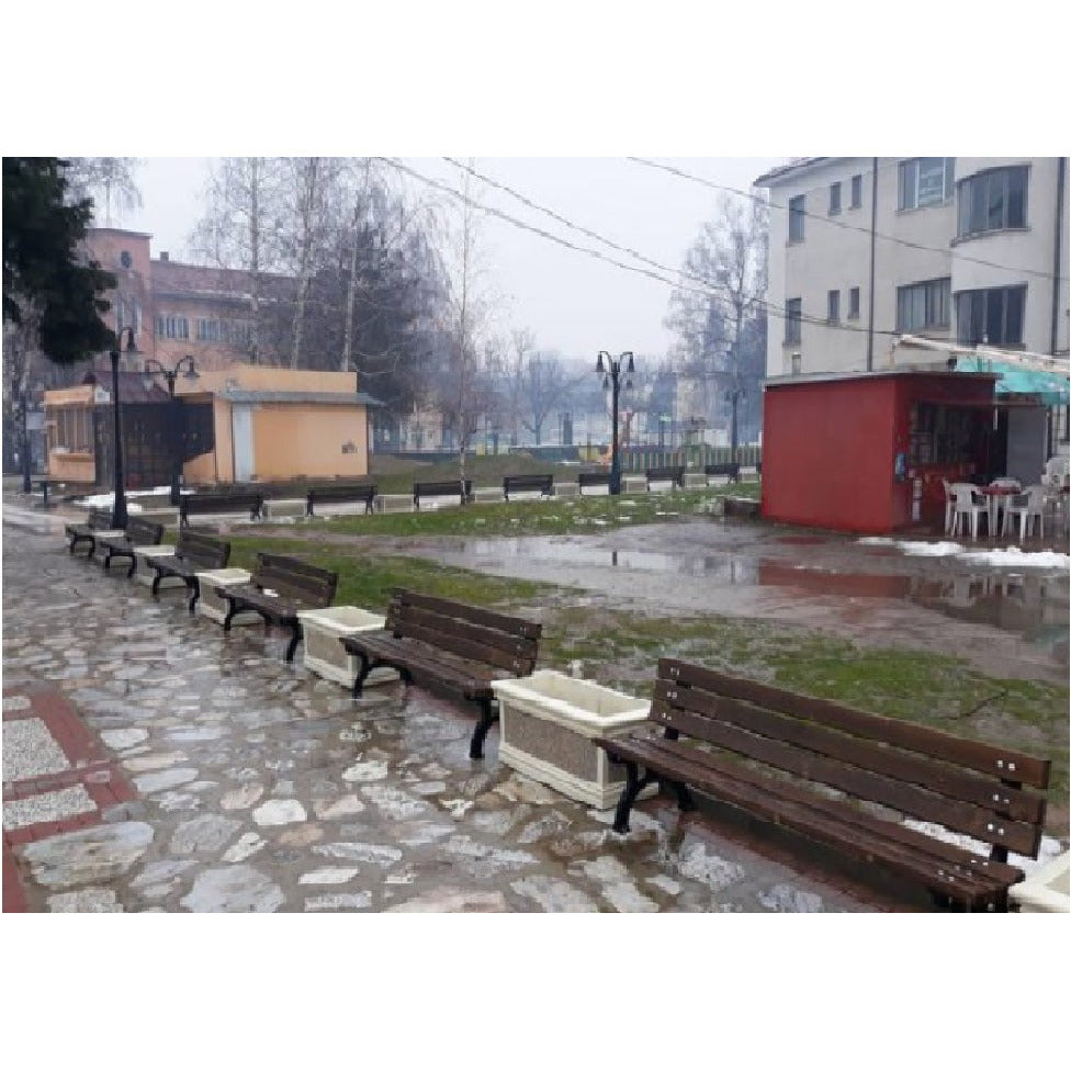 Пейка в градска среда, на фона на дъждовен ден, с мокра настилка и зелена тревна площ.