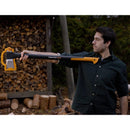 Брадва за цепене на дърва Fiskars X27 XXL, мъж държи инструмент за цепене на дърва на фон с нарязани трупи.