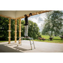 Мъж работи на алуминиева регулирана платформа WERNER на открито, с красиви дървета и мебели на фона.