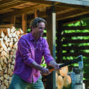 Мъж, който цепи дърва с брадва Fiskars X17 M в дървена пристройка сред купчини с дърва.