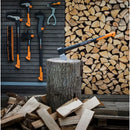 Брадва за цепене на дърва X21 L на дънер с нарязани трупи и инструменти на стена в бекграунда.