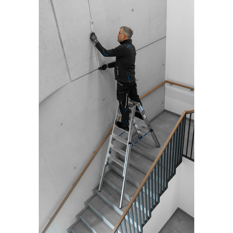 Професионалист използва алуминиева телескопична стълба Krause STABILO за работа на тясно стълбище.