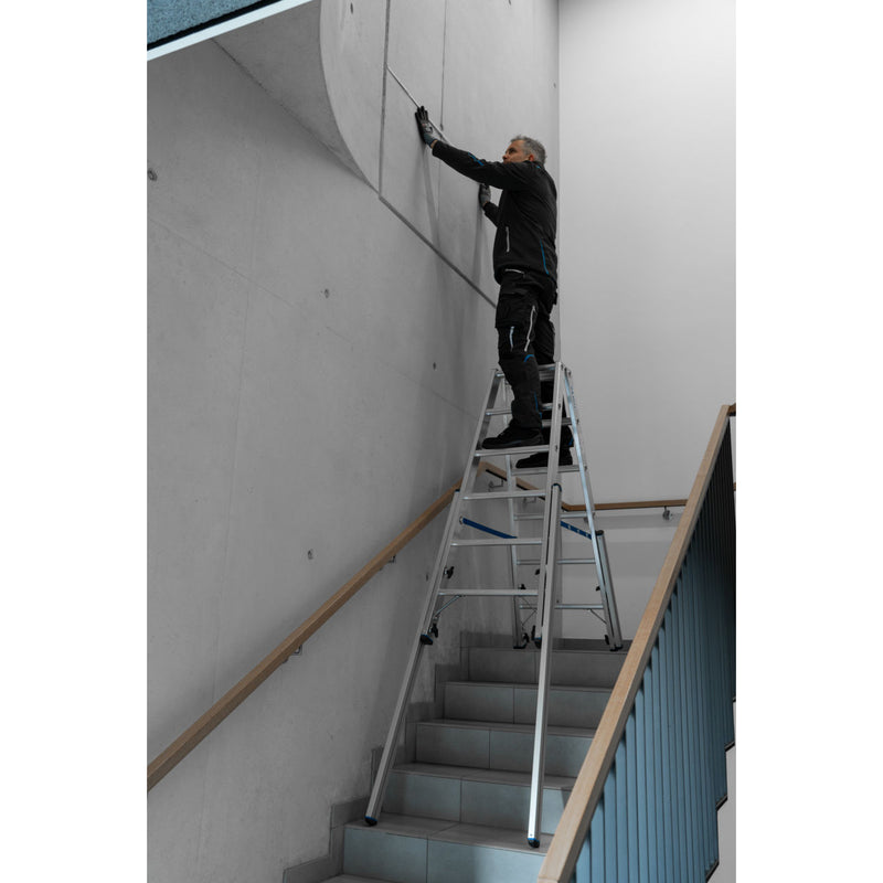 Професионалист работи на алуминиева телескопична стълба Krause STABILO на стълбище.