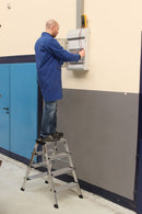 Човек на двустранна алуминиева стълба KRAUSE TREPPO, работещ на стена за електрически монтаж.