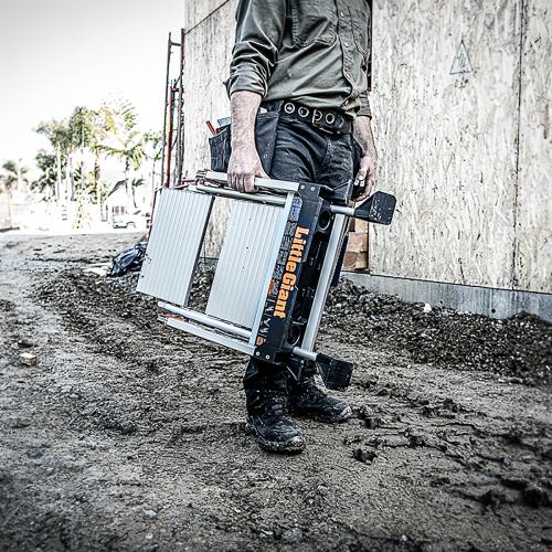 Мъж държи алуминиева стълба Little Giant Jumbo Step на строителен обект, демонстрираща лекота и стабилност.