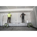Двама работници върху телескопична дъска Telescoping Plank™, боядисващи стена в строителен обект.