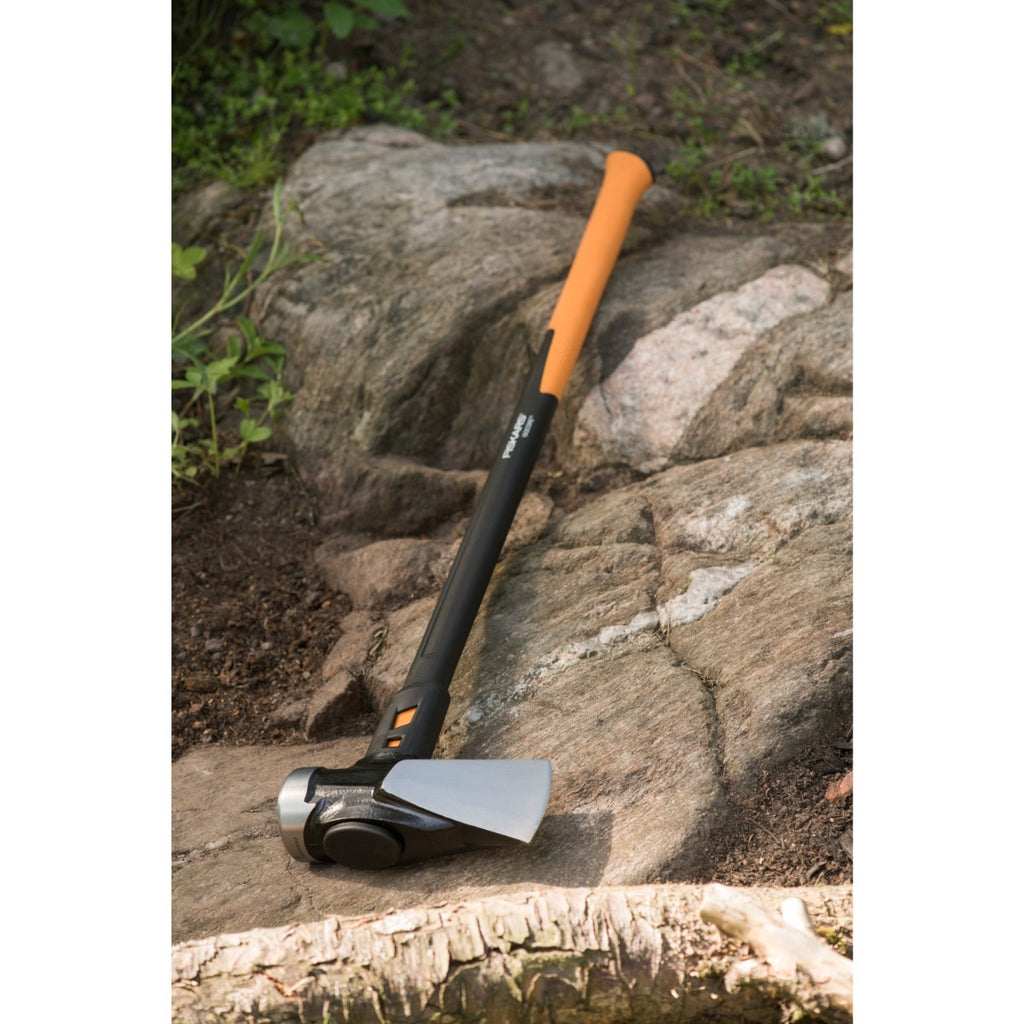 Alt Tag: Чук за цепене Fiskars IsoCore™, размер XXL лежи на скала с кована стоманена глава и оранжева дръжка