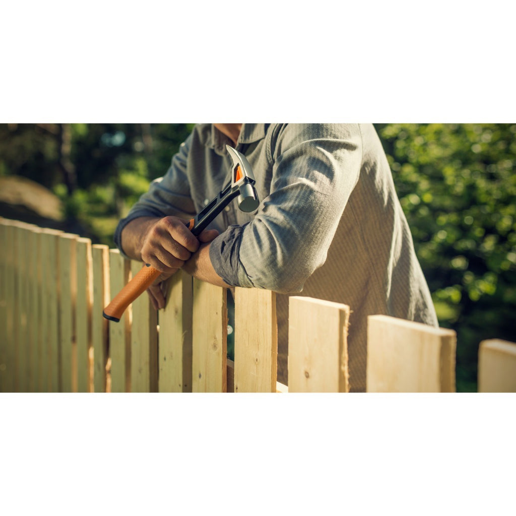 Универсален чук Fiskars IsoCore™ размер L в ръка на дърводелец при монтаж на дървена ограда