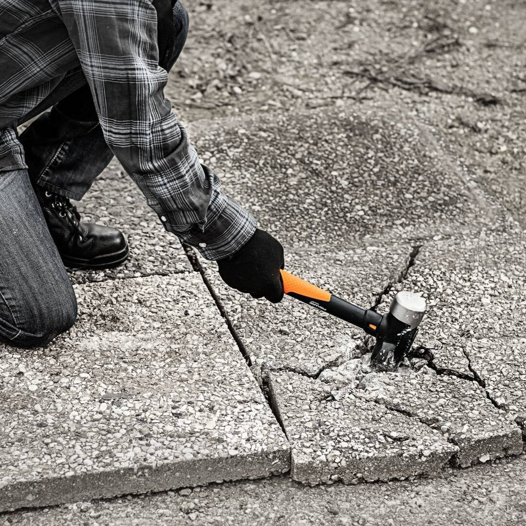 Строителен чук Fiskars IsoCore™ размер L в действие при чупене на бетонна настилка с анти-вибрационна дръжка