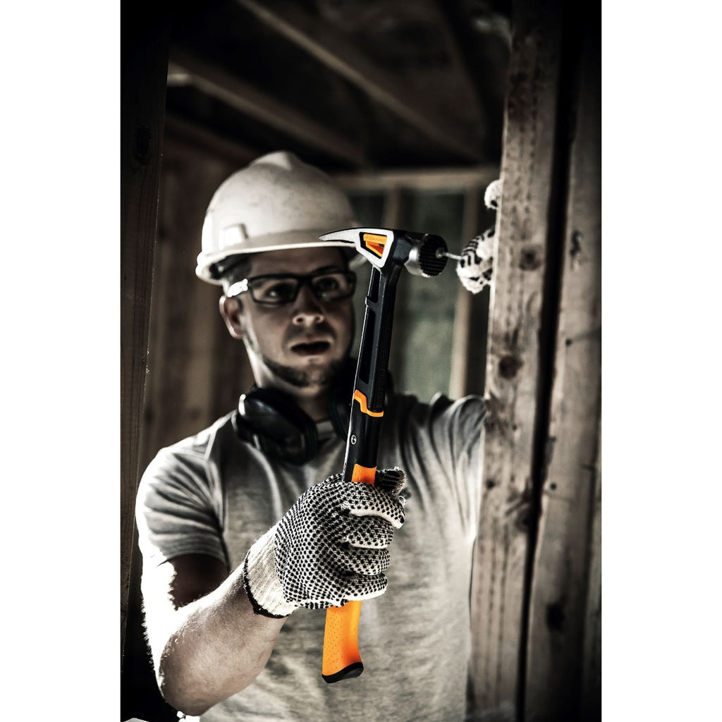 Кофражен чук с магнитна глава Fiskars IsoCore™ 0.624 kg, размер XXL показан в ръка на строител с каска и ръкавици