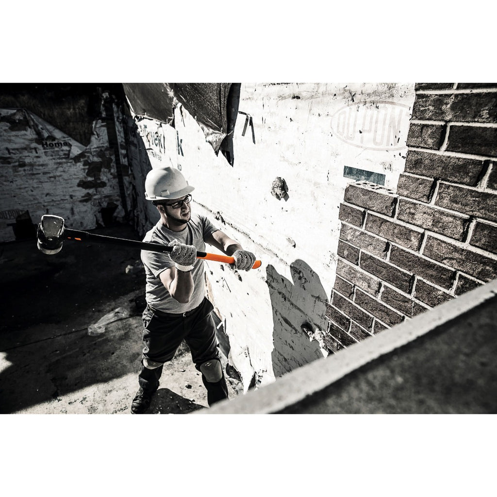 Чук за разбиване и къртене Fiskars IsoCore™ 4.76 kg размер L в действие, работник с предпазна каска и дълга дръжка ударя стена