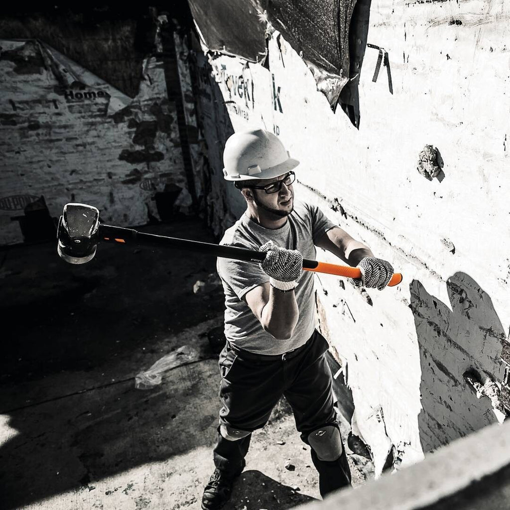 Чук за разбиване и къртене Fiskars IsoCore™ 5.76 kg размер XL в употреба от работник с предпазна каска и ръкавици за къртене