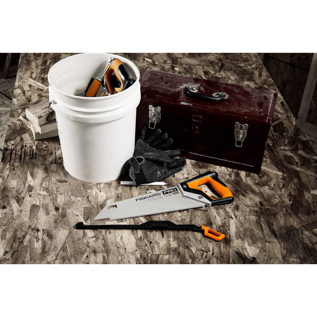 Трион Fiskars PRO PowerTooth (38 см, 9 TPI) с тройно заточено острие и оранжева дръжка върху работна настилка до кофа и инструментална кутия