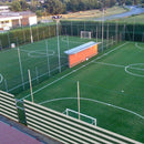 Изглед отгоре на футболни игрища с мрежа и сграда за съблекални на спортен комплекс.