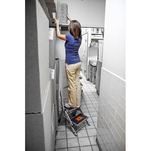 Жена използва стълба с две стъпала SAFETY STEP МАЛКИЯ ГИГАНТ® за достигане на високи рафтове в кухня.