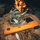 Брадва Fiskars X5 на дърво с огън на заден план, идеална за къмпинг и туризъм.