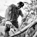 Мъж работи с брадва в природата, подготвяйки се за къмпинг или лов.