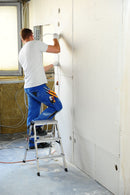 Работник на двустранна алуминиева стълба KRAUSE DOPPLO, боядисва стена в ремонтирано помещение.
