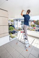 Мъж използва алуминиева стълба KRAUSE Sepuro на тераса за извършване на ремонтни задачи.