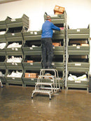 Човек стои на стълба с 4 стъпала, достигайки до високи рафтове в склад.