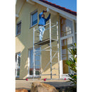 Мъж работи на алуминиево мобилно скеле KRAUSE CORDA в градината, демонстрирайки немско качество и лесно транспортиране.