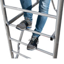 Човек стои на стъпала на алуминиево скеле, демонстрирайки стабилност и безопасност при работа на височина.