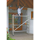 Човек на алуминиево мобилно мини скеле KRAUSE, боядисващ таван, демонстриращо немско качество и лесно транспортиране.