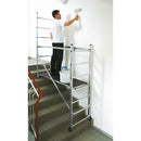 Работник използва алуминиево мини скеле KRAUSE за боядисване на стена в стълбище, демонстриращо немско качество и лесно транспортиране.