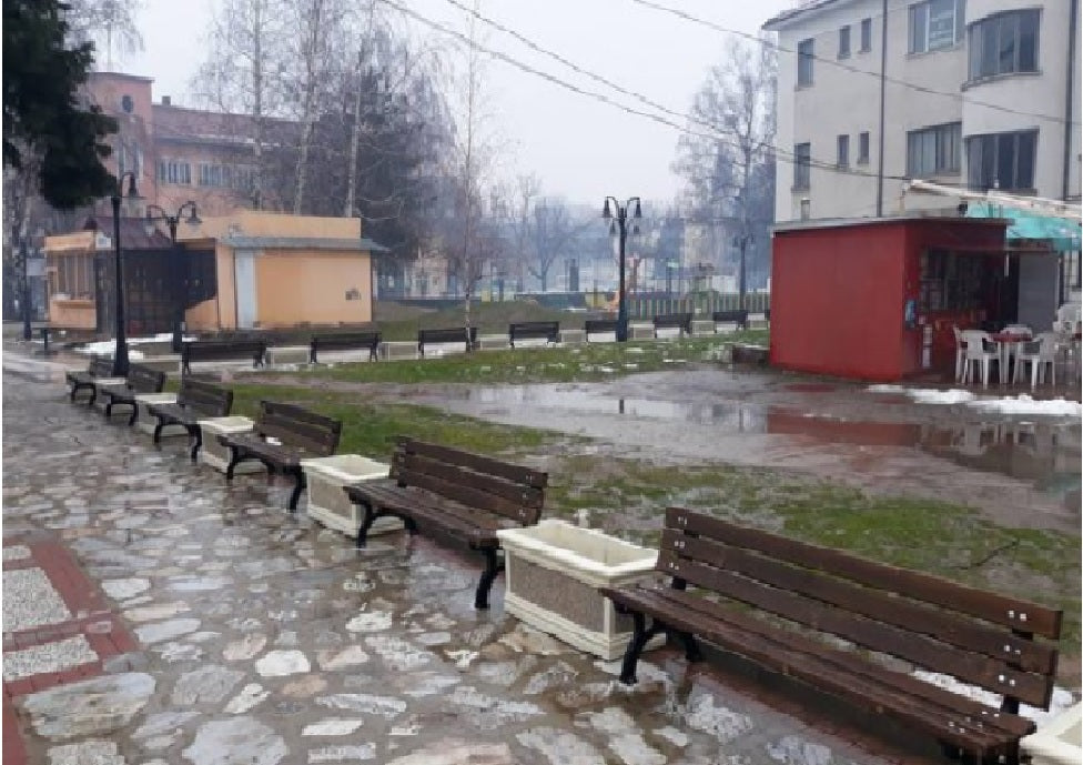 Пейка в градска среда, на фона на дъждовен ден, с мокра настилка и зелена тревна площ.