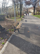 Дървени пейки в парк, разположени по алея сред дървета и зелена тревна площ.